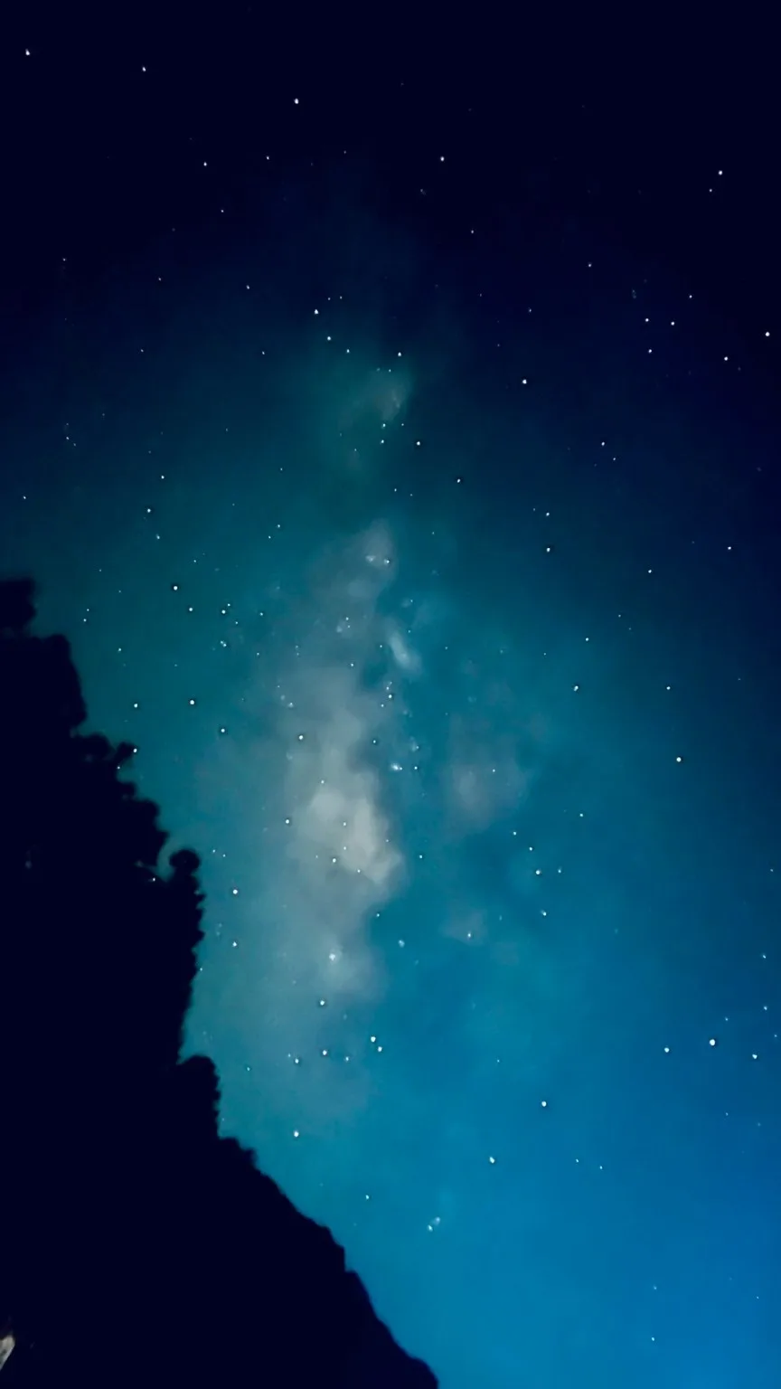 The Milky Way photographed with a smartphone. A faint white cloud-like band of light floats among the stars.